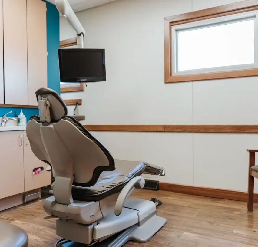 A dental exam room with an empty chair, a mounted screen, and storage cabinets.