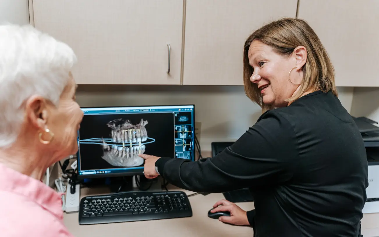 A woman shows an elderly woman dental images on a computer screen in a dental office.