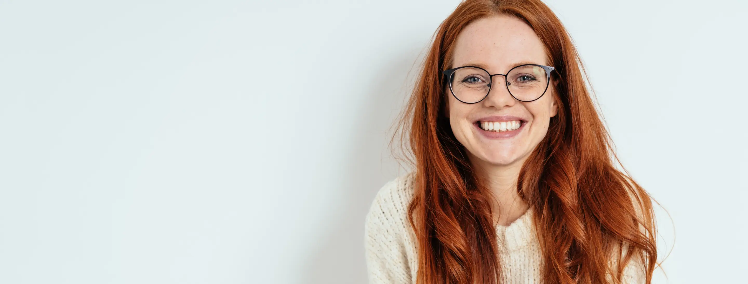 A person with long red hair and glasses is smiling at the camera.