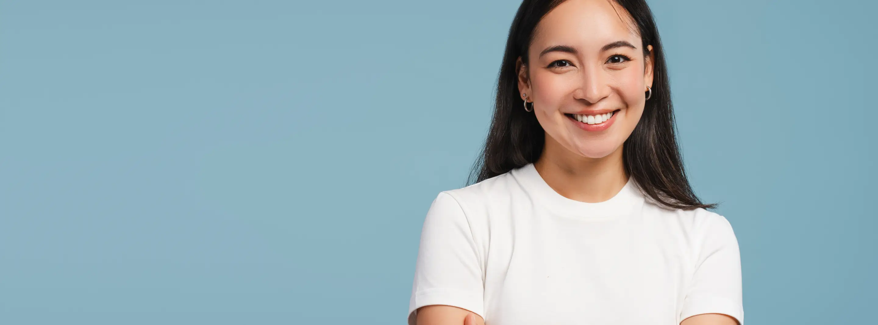 Smiling woman in a white shirt standing against a plain blue background.