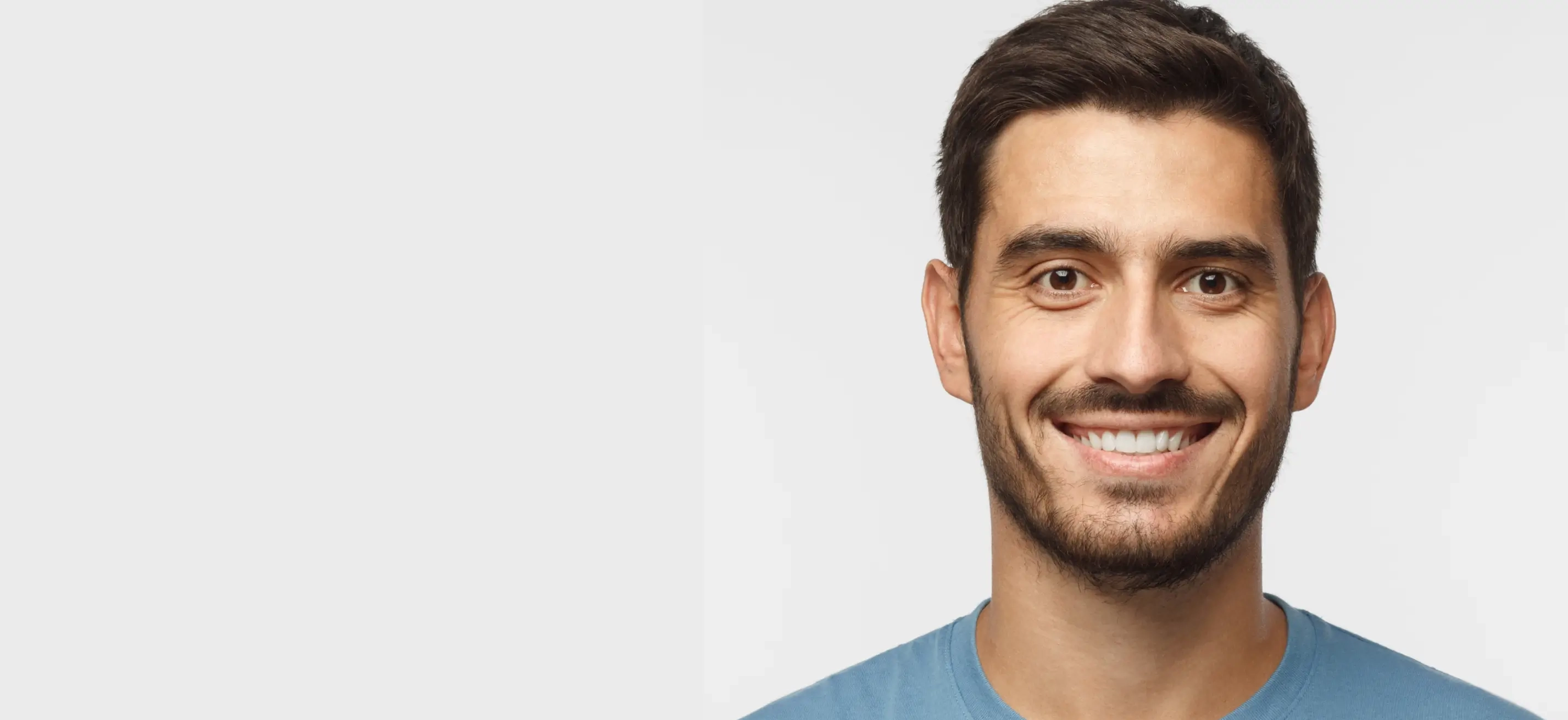 A man with short brown hair and a beard, smiling at the camera, wearing a blue shirt.
