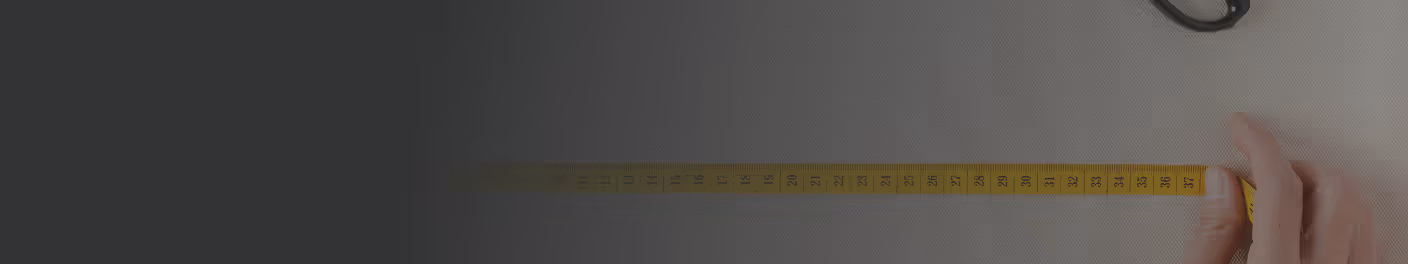 Hand holding a yellow measuring tape stretched out on a light surface with scissors nearby.
