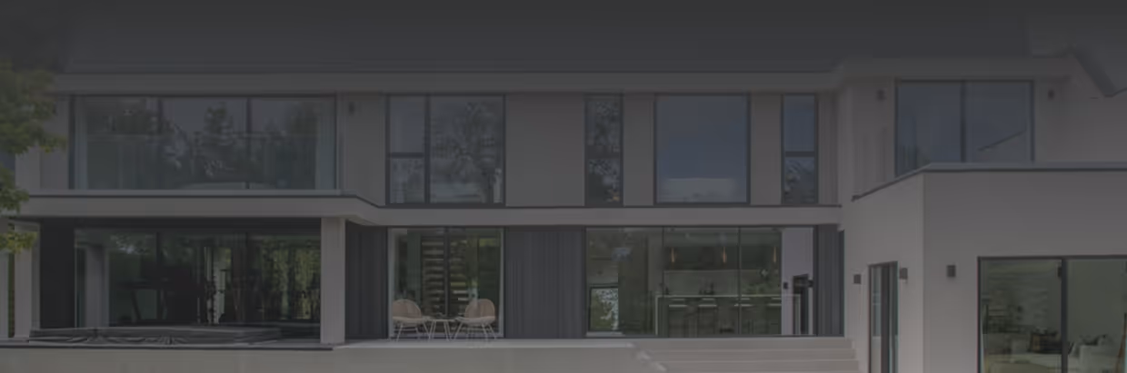 Modern two-story house with large glass windows, outdoor seating area, and a light-colored patio.