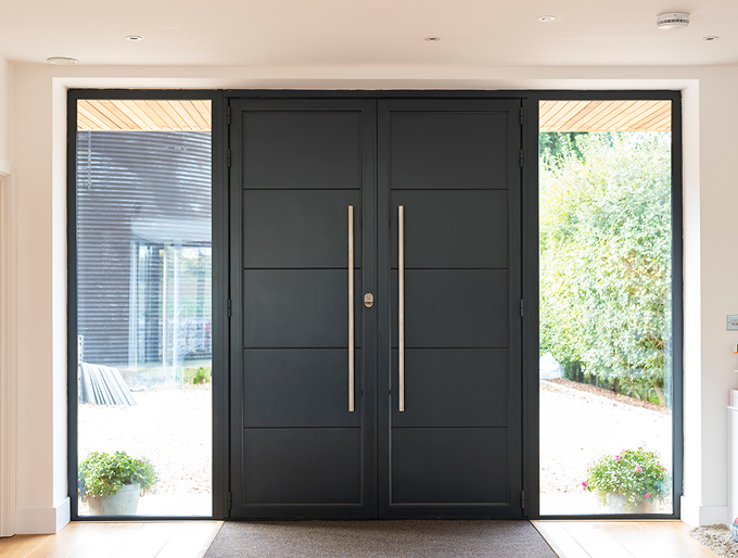 Modern black double entrance doors with large vertical handles and glass panels on both sides showing outdoor garden and pathway.