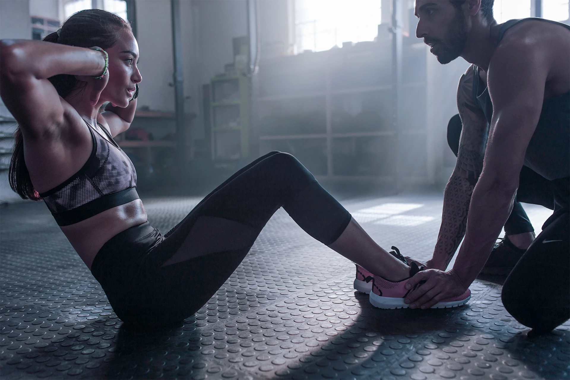 Personal trainer supports gym goer doing sit-ups.
