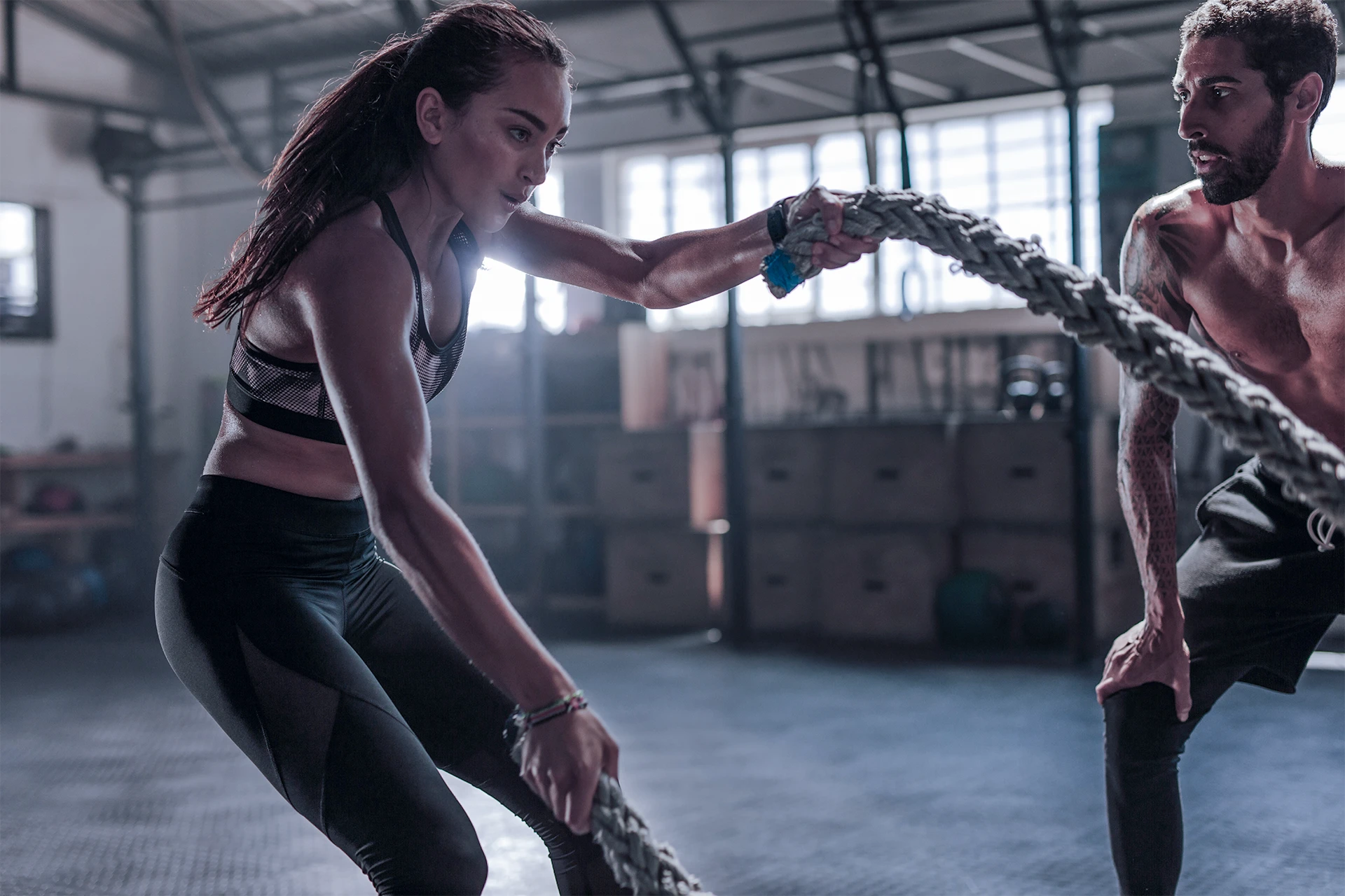 Personal trainer encourages gym goer exercising with battle ropes.