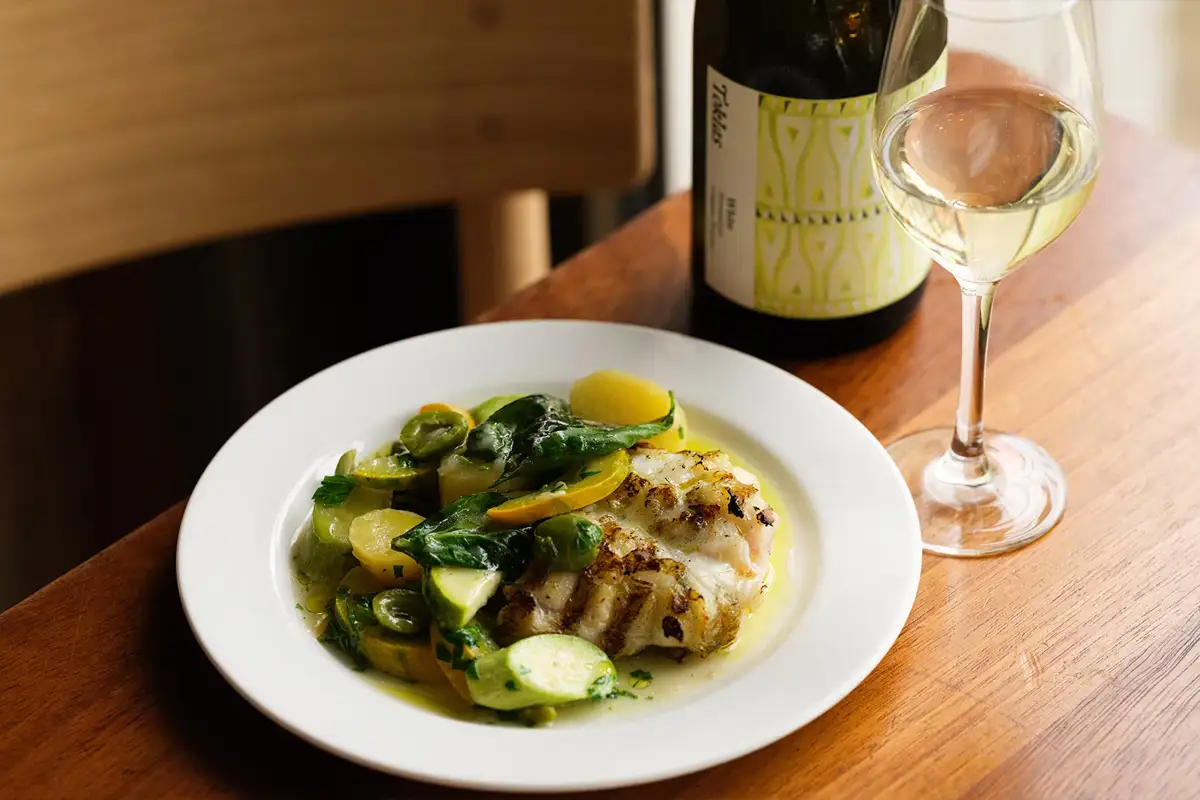 Chicken with new potatoes, courgette with glass of white wine along with the bottle in the background