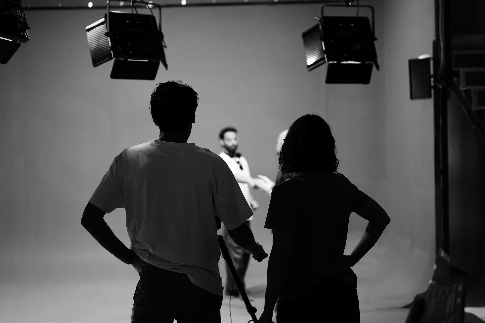 Dos personas de espaldas observan a dos hombres charlando en un estudio con luces de rodaje.