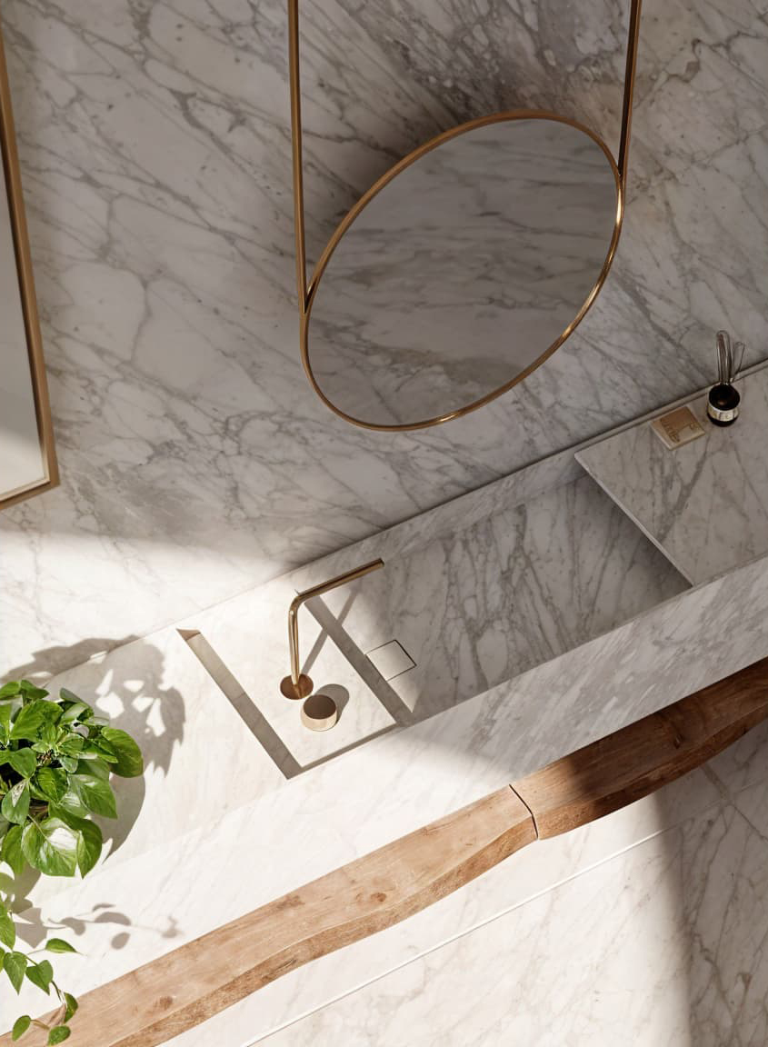 Lavabo y pared de mármol con grifo dorado, espejo redondo y planta verde moderna.