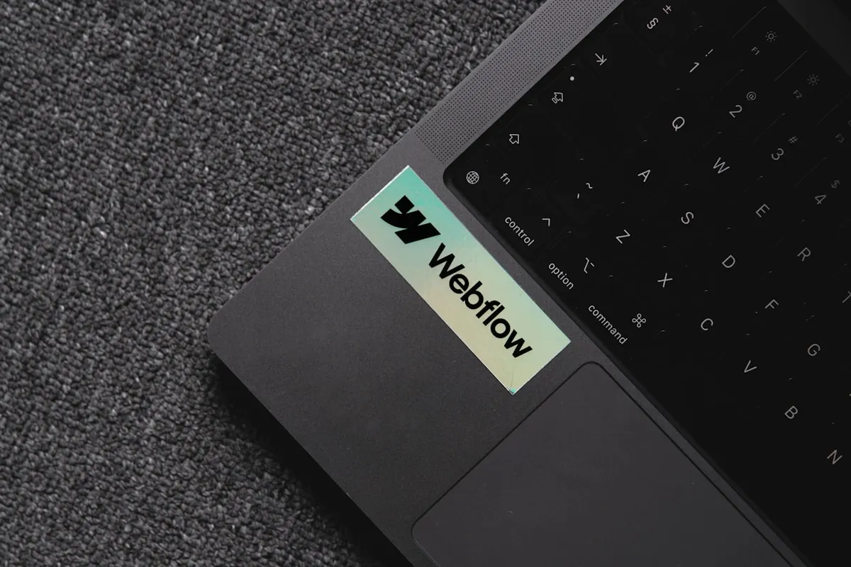 Close-up of a laptop palm rest with a holographic Webflow sticker near the keyboard.