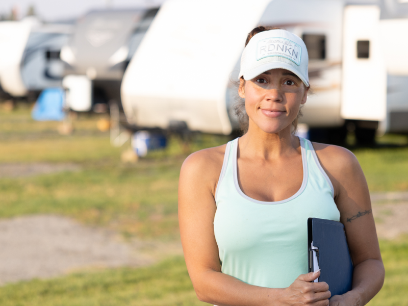 A women with a ball cap is holding a clipboard and standing in front of a row of recreational vehicles.
