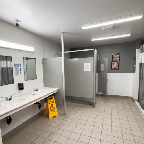 Washroom interior showing clean sinks, toilet stall and shower curtain.