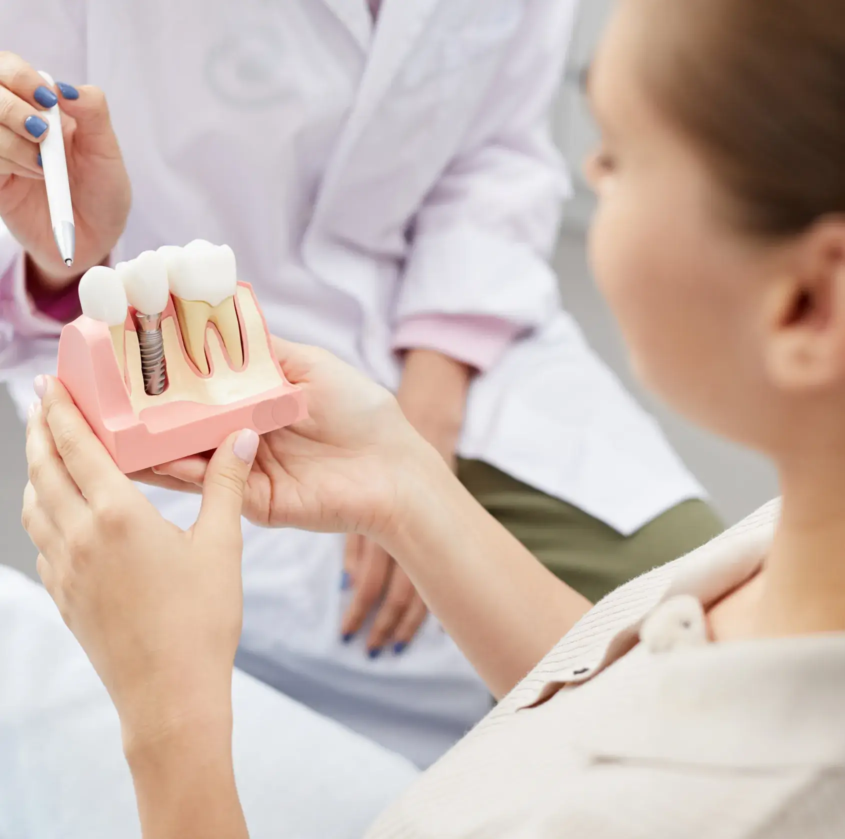 Dentist explaining a dental implant model to a patient using a pen pointer.