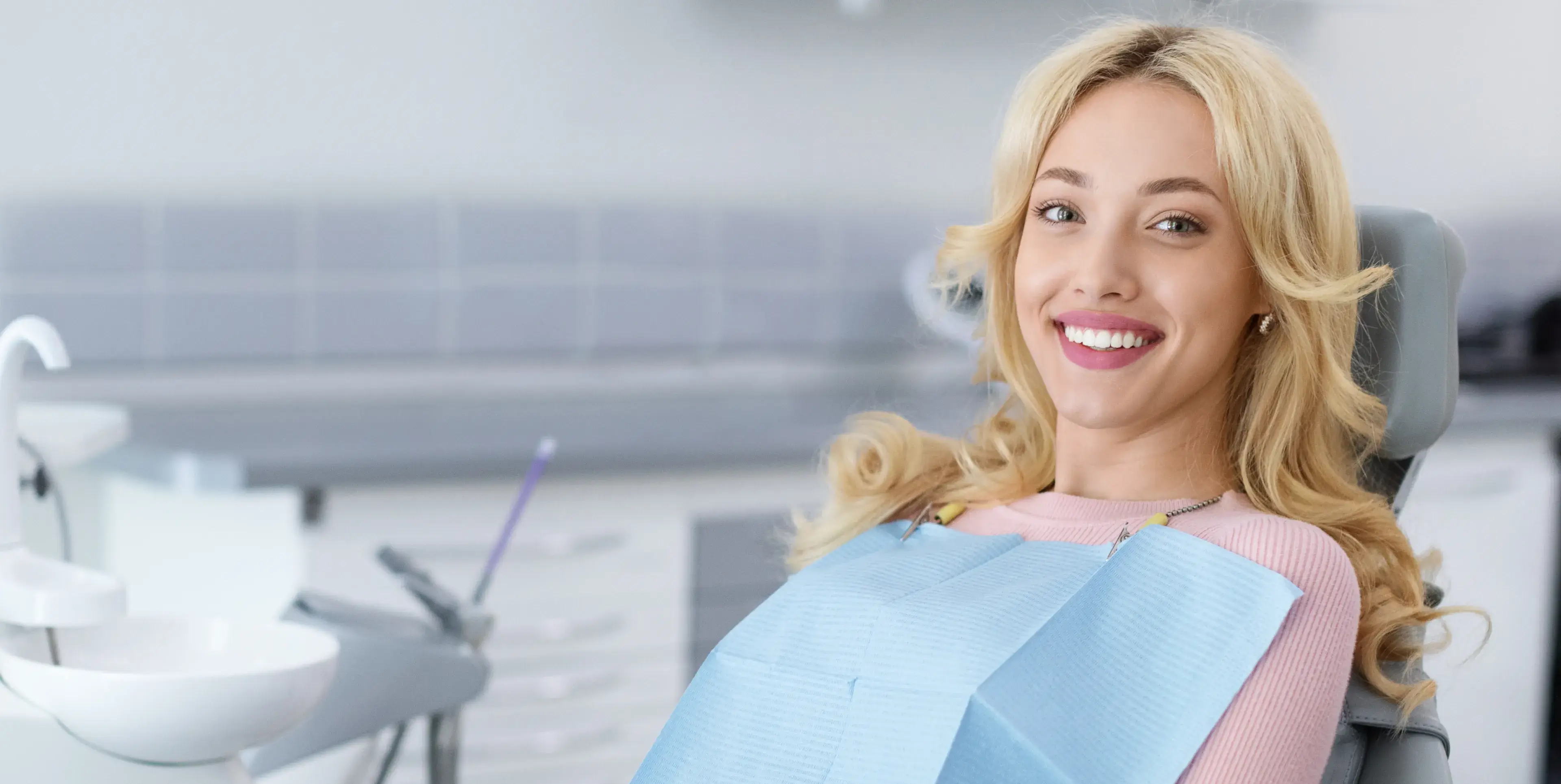 Smiling blonde woman sitting in a dental chair wearing a blue dental bib.