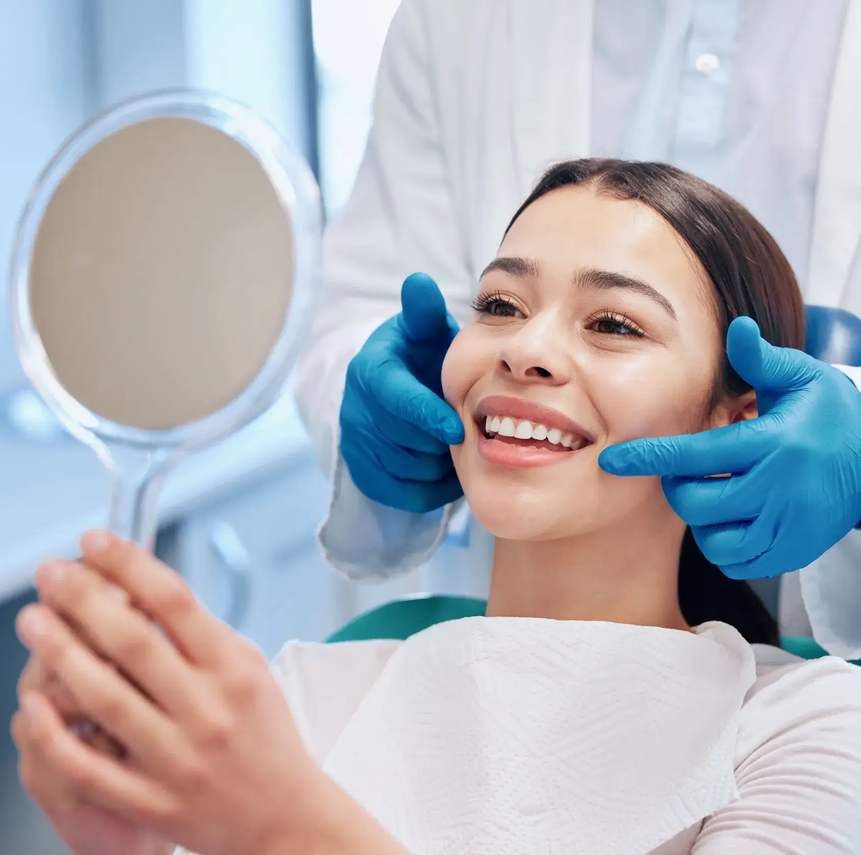 Smiling woman holding a mirror while a healthcare professional wearing blue gloves examines her cheeks.