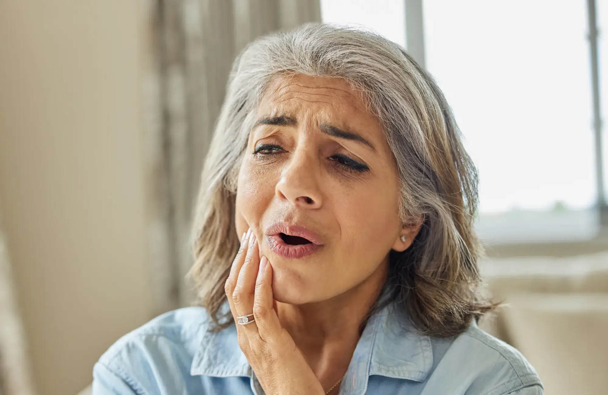 Middle-aged woman with gray hair holding her jaw in pain, appearing to have a toothache.