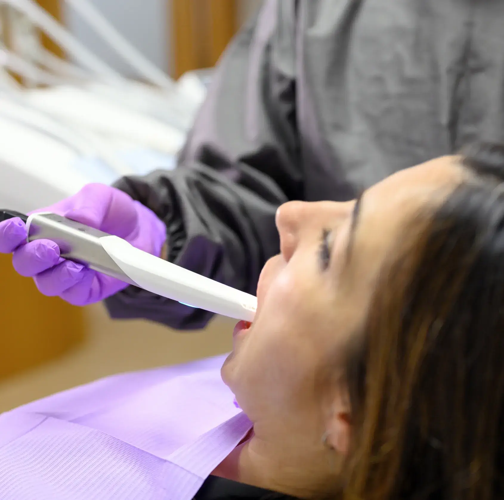 Close-up of a woman receiving a dental scan with an intraoral scanner held by a gloved hand.