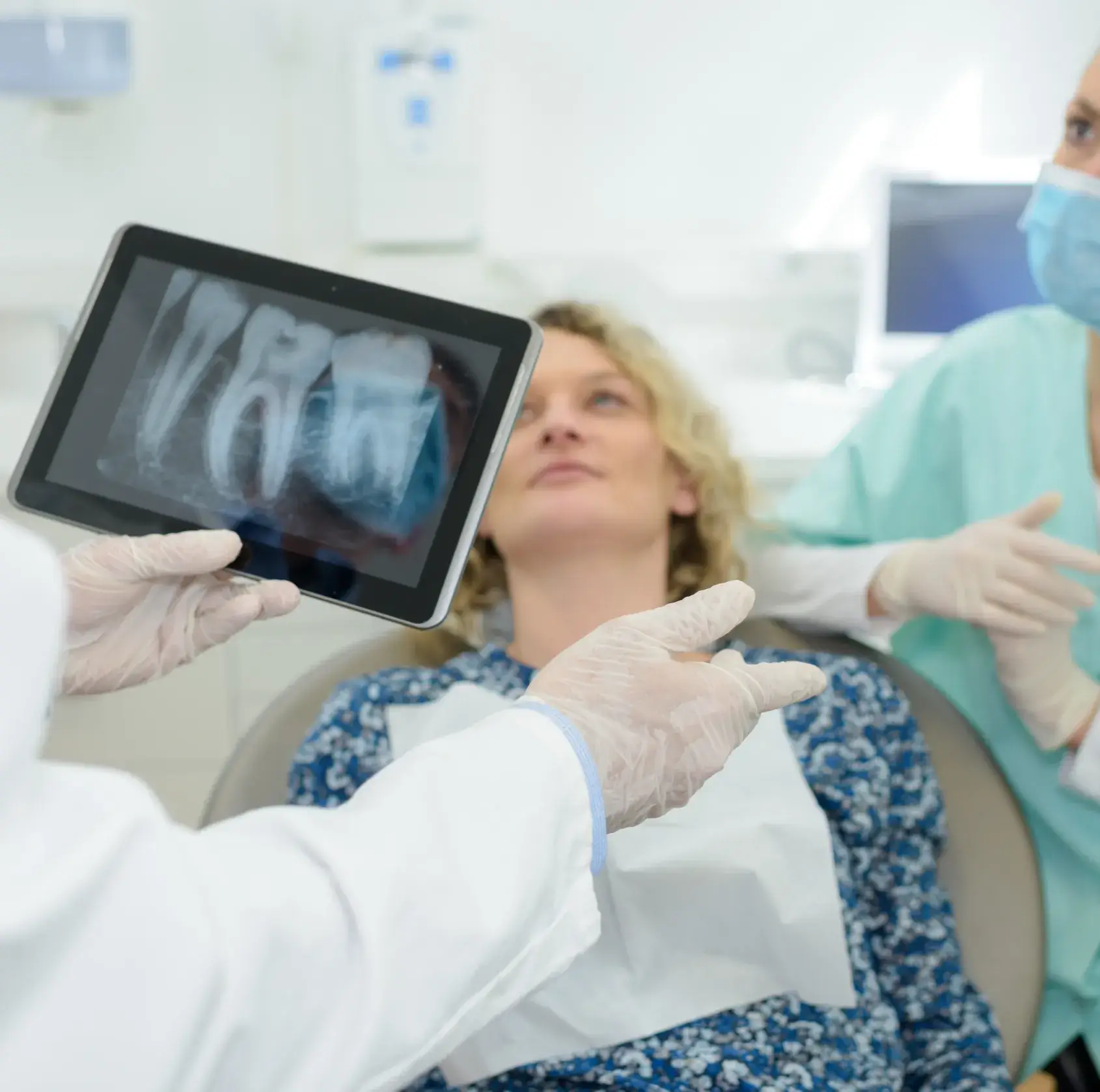 Dentist showing a dental X-ray on a tablet to a seated female patient in a dental clinic.