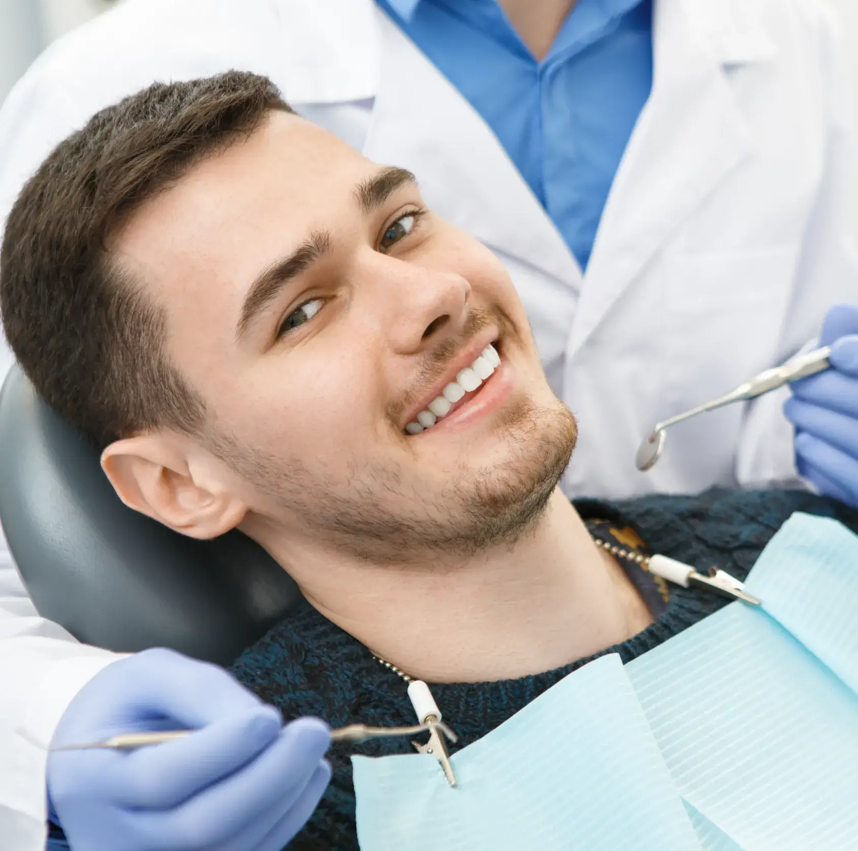 Smiling young man reclining in dental chair during a checkup with a dentist holding dental tools.