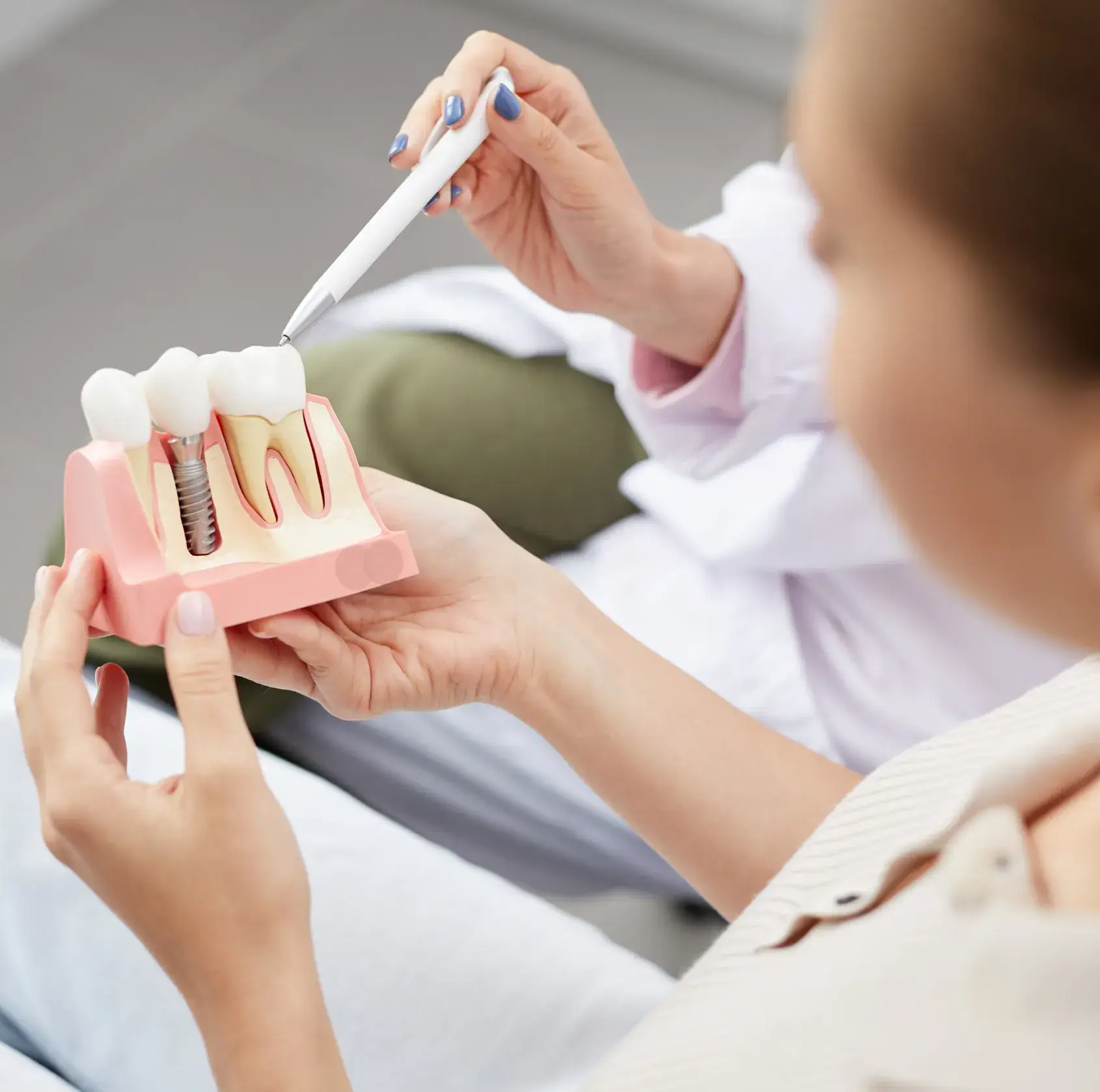 Dentist using a pen to explain a dental implant model to a patient.