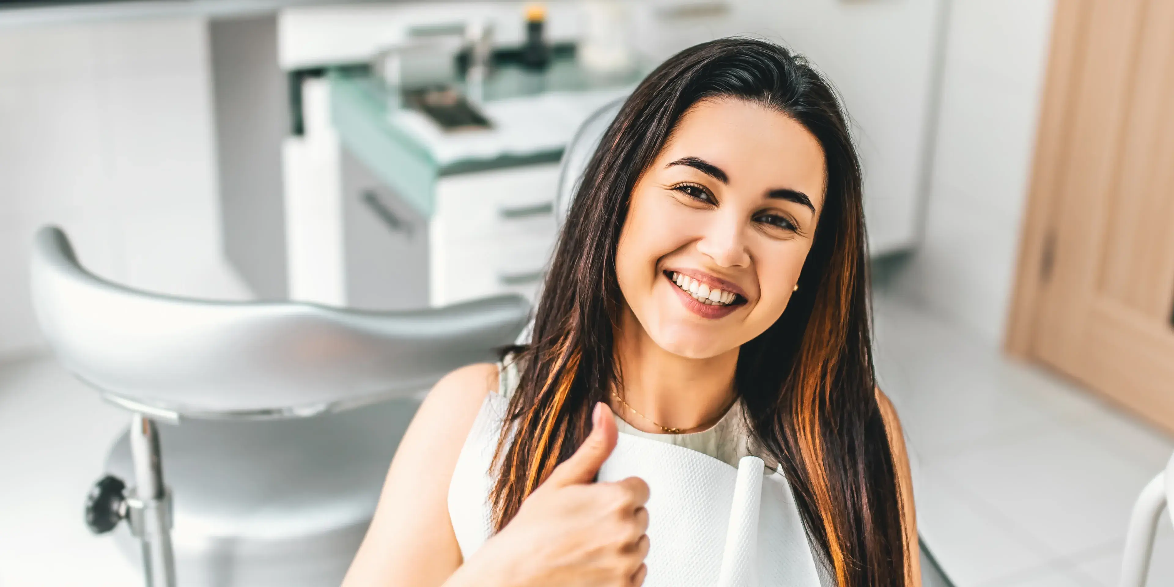 Smiling woman in dental chair giving a thumbs-up after a dental checkup.