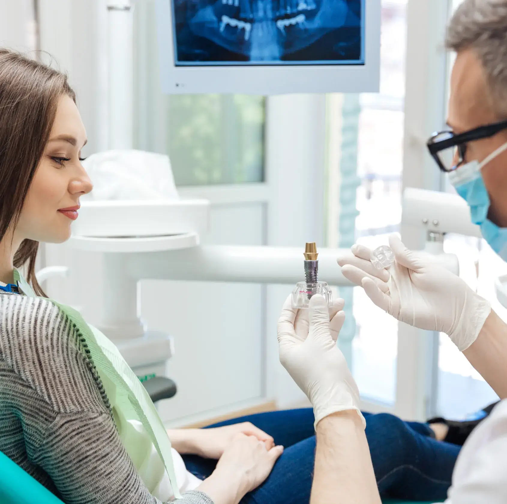 Dentist showing a dental implant model to a female patient in a dental office.