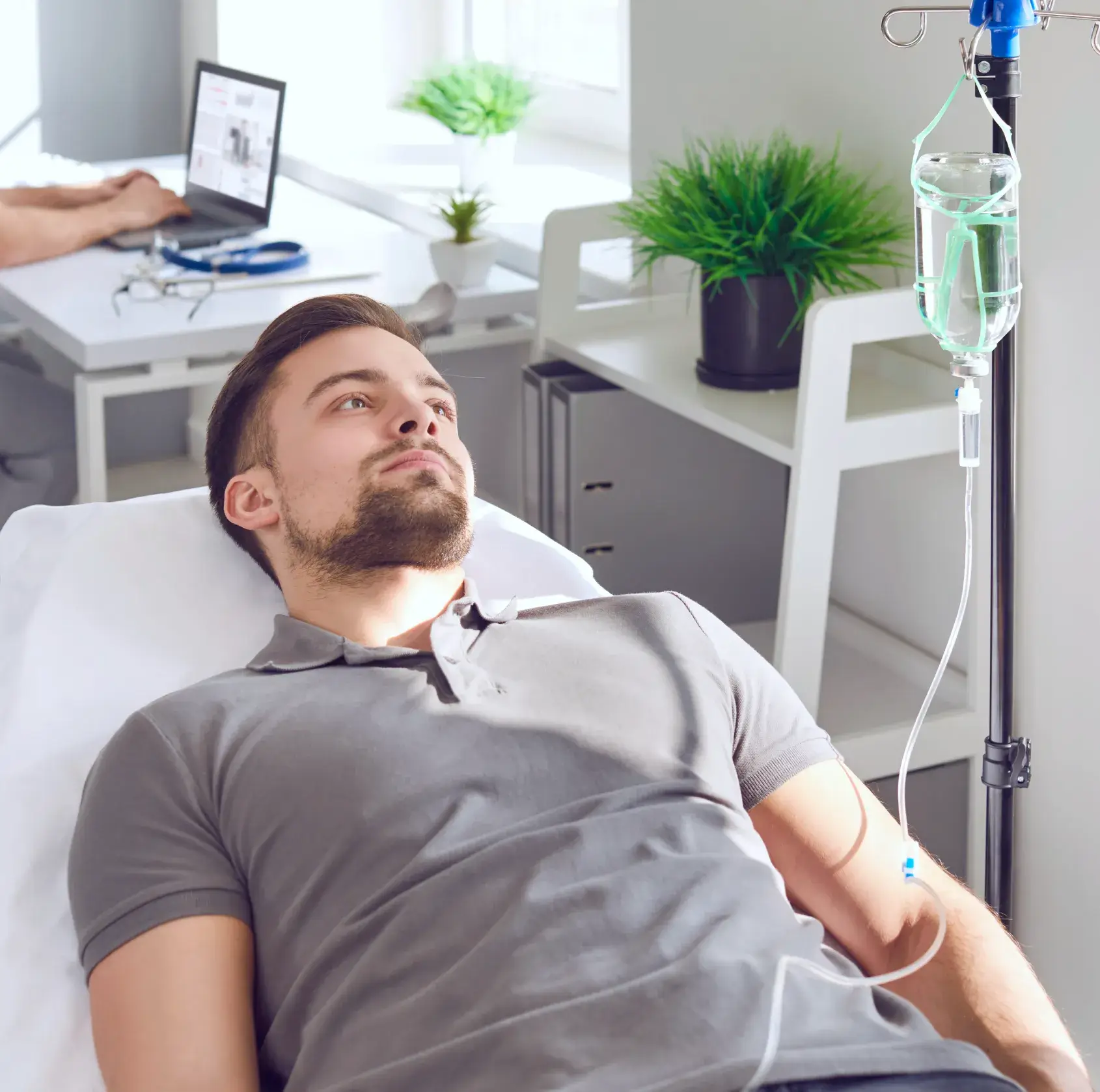 Young man lying on a hospital bed receiving intravenous therapy with IV drip in a bright medical room.