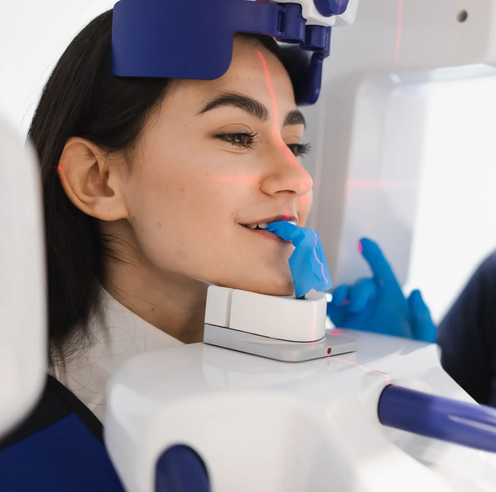 Woman undergoing a dental or medical imaging scan with a blue bite block and red alignment laser lines on her face.