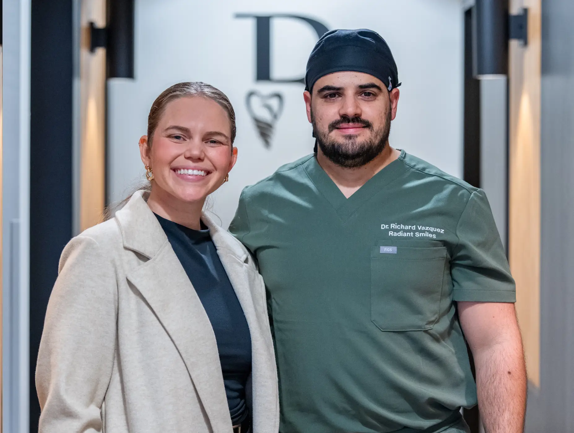 Three smiling dental professionals standing indoors, with the man in the center wearing green scrubs labeled Dr. Richard Vazquez Radiant Smiles.
