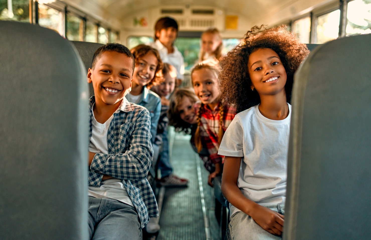 Smiling diverse children sitting inside a school bus looking towards the camera.