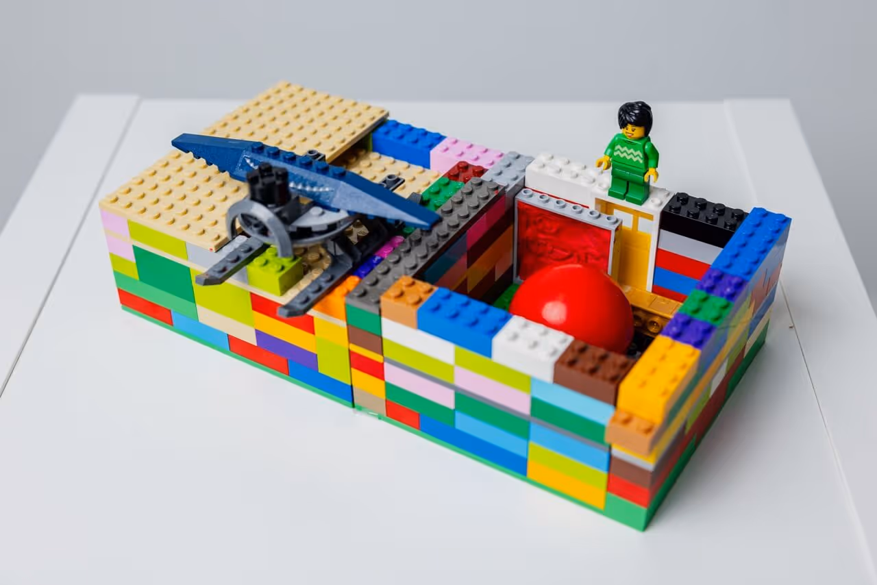 Colorful Lego structure with a large red ball inside surrounded by a block wall and a Lego figure in green standing on top.