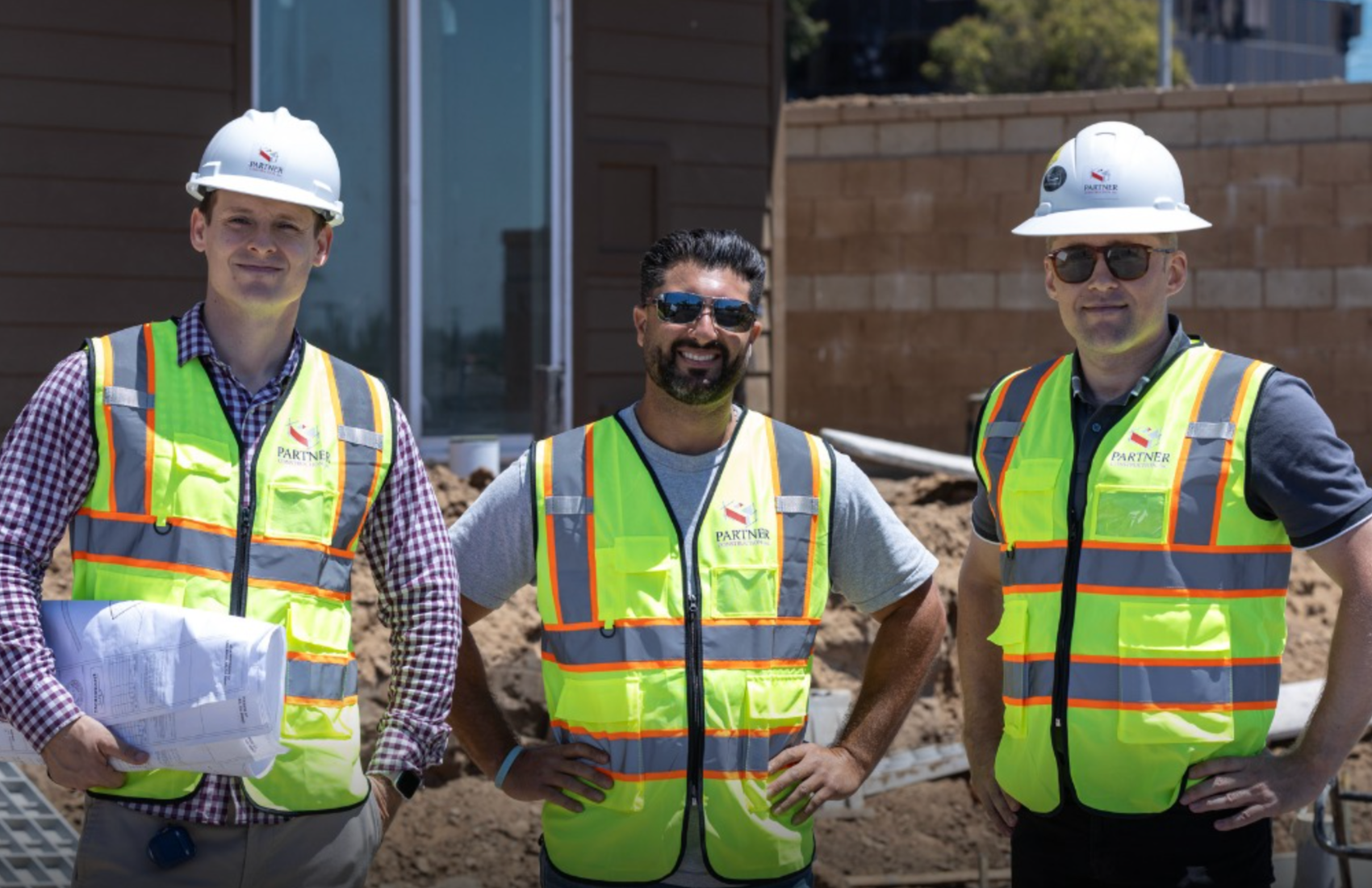 Three construction workers in safety vests and hard hats on job site