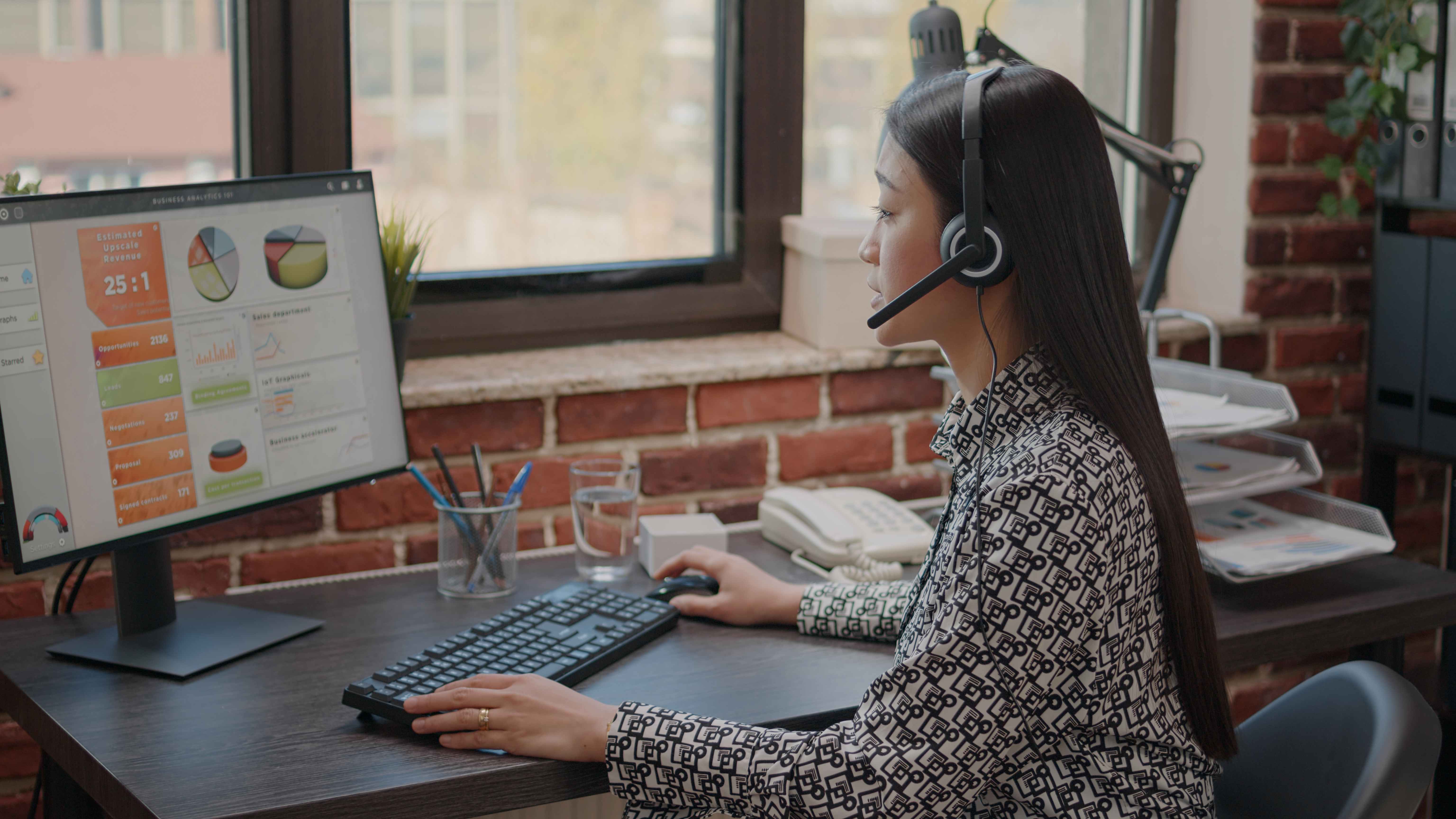 Woman with headset analyzing business data charts on computer monitor