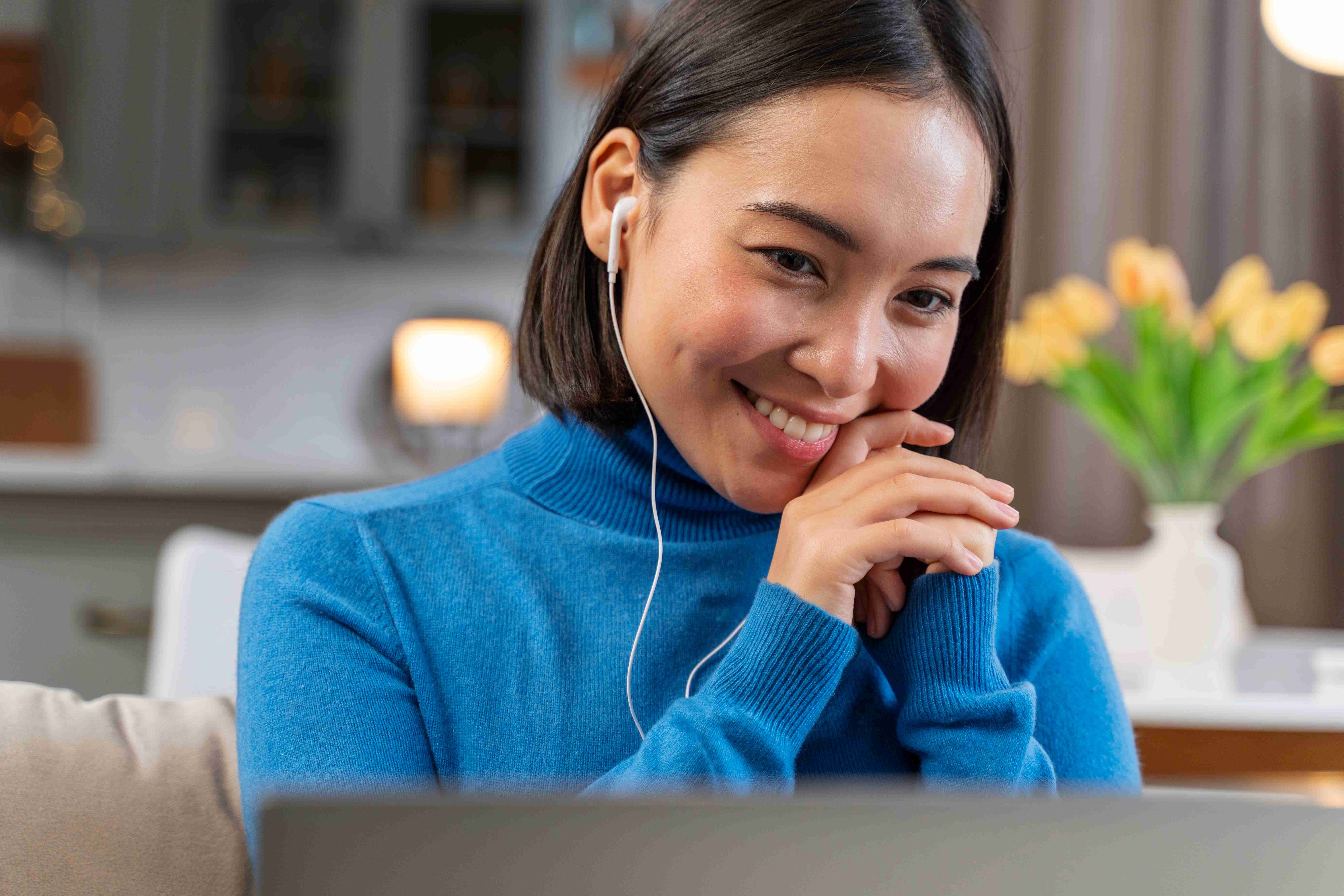 Smiling woman in blue sweater wearing earphones, sitting at home