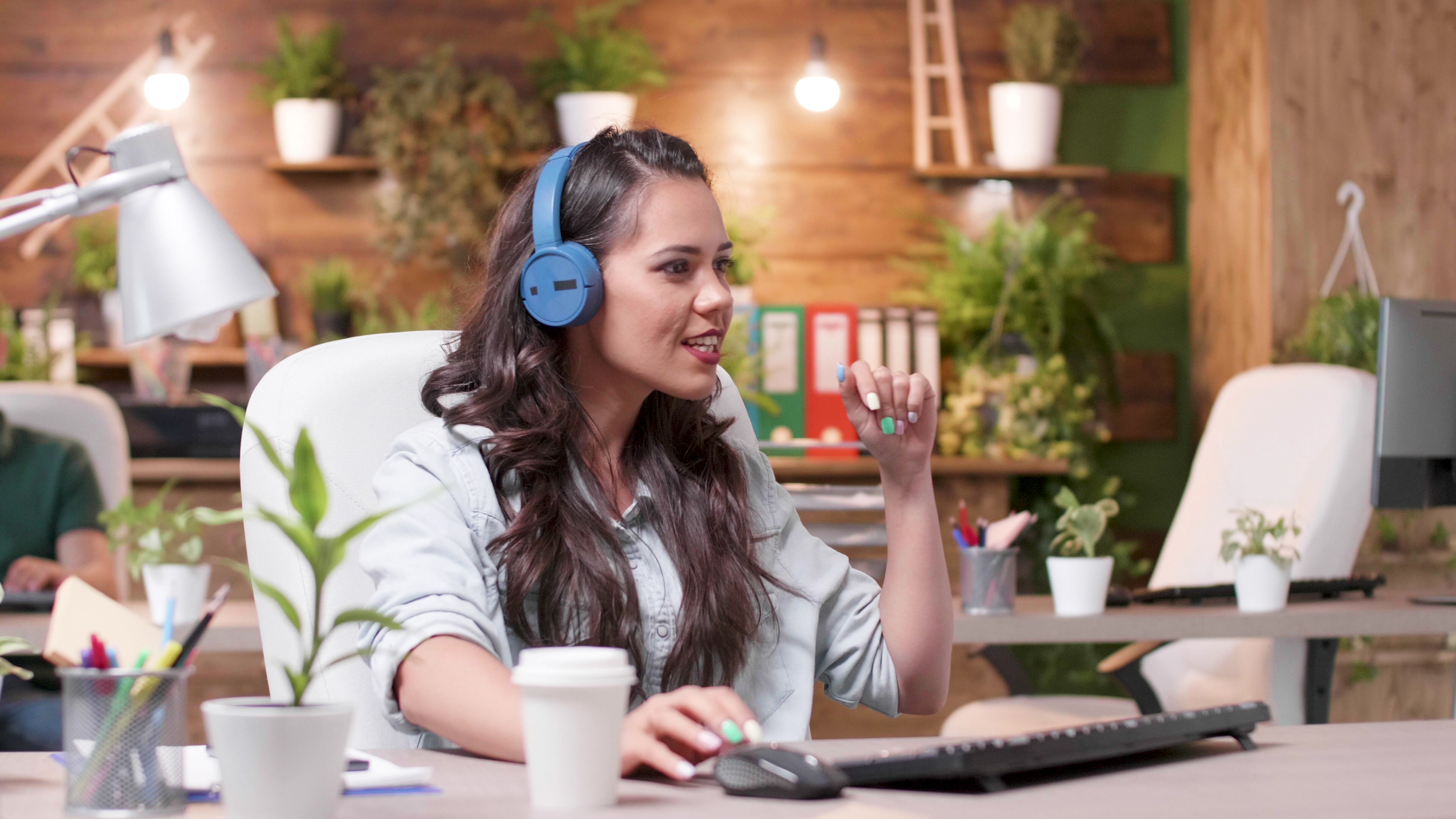 Woman with blue headphones working in green plant-filled modern office