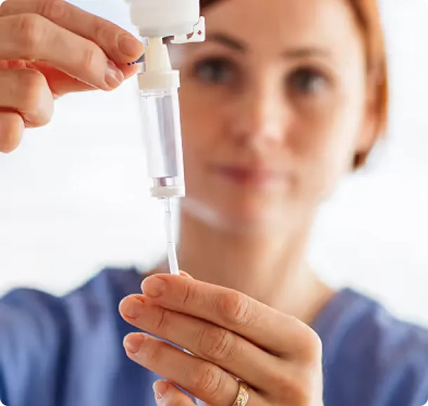 Nurse adjusting an intravenous drip chamber with clear fluid.