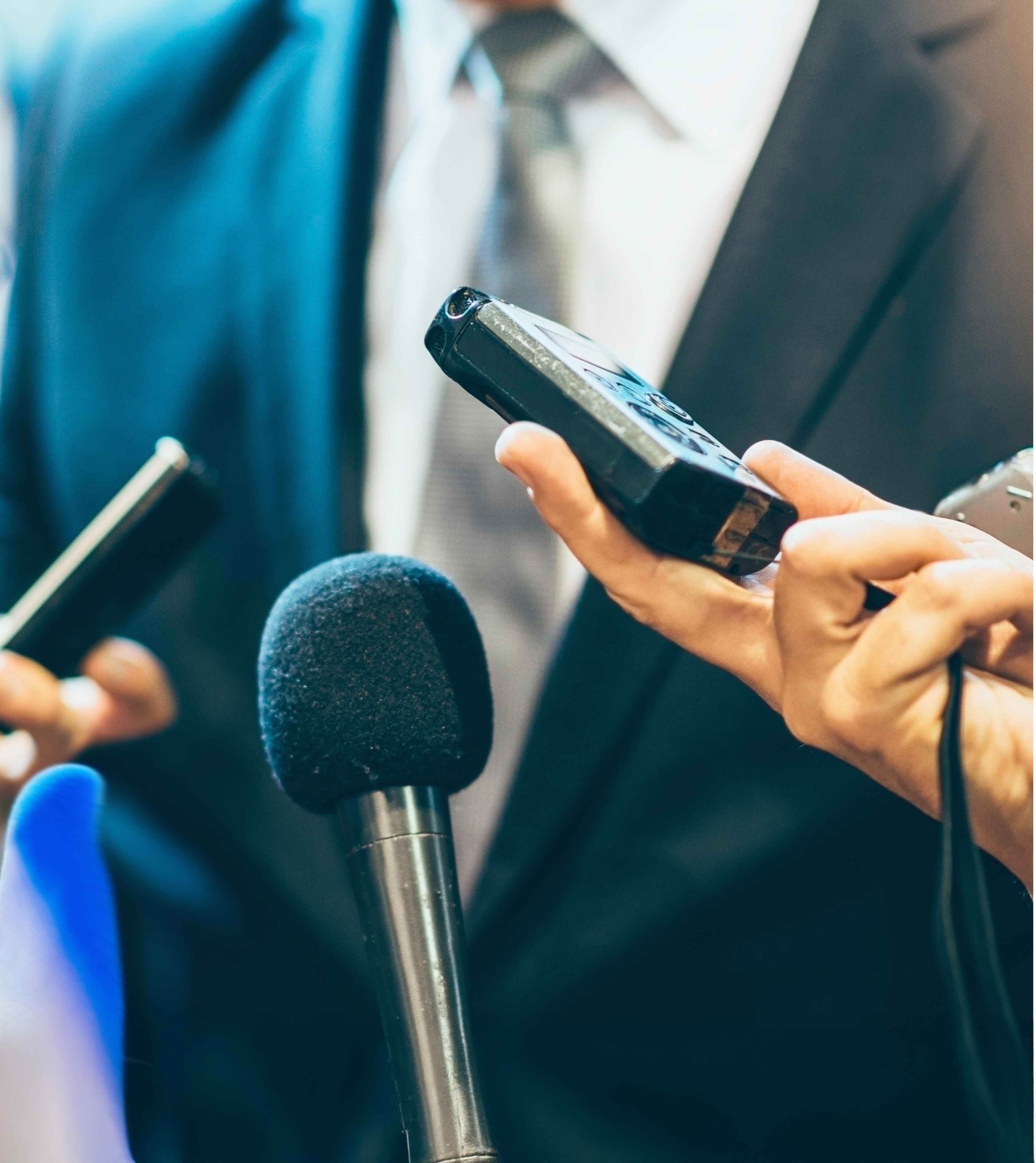 Close-up of a journalist holding a digital recorder and surrounded by microphones during an interview.