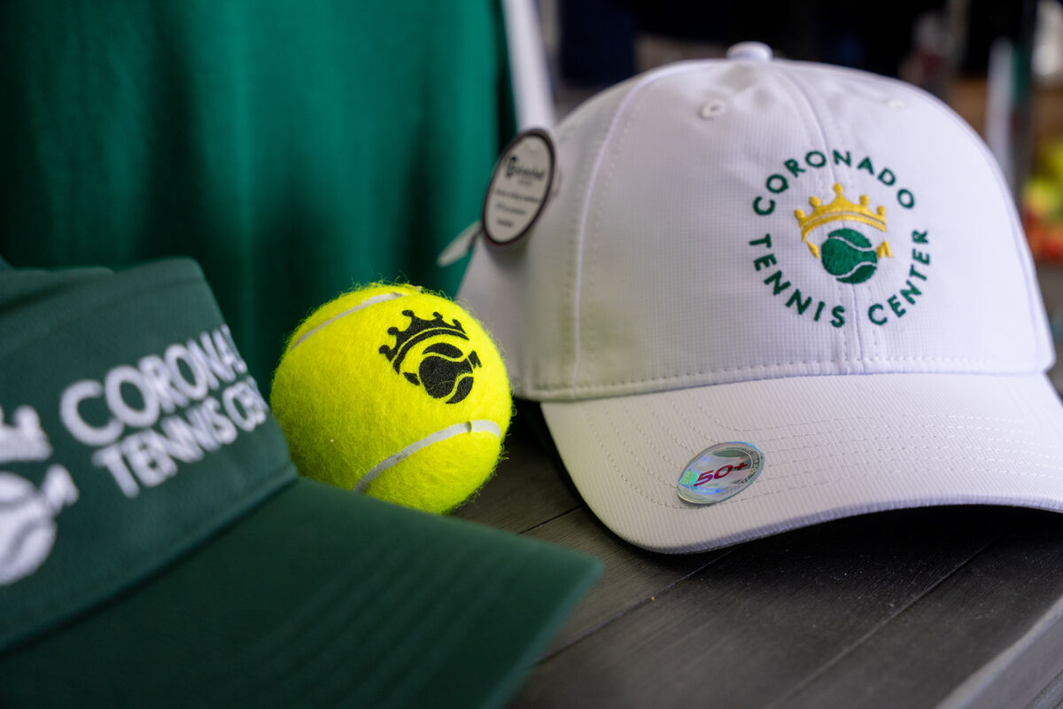 Close up of a baseball cap, a tennis ball and a visor hat with Coronado Tennis' logo on them.