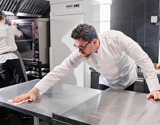 Kitchen staff cleaning a commercial food preparation surface