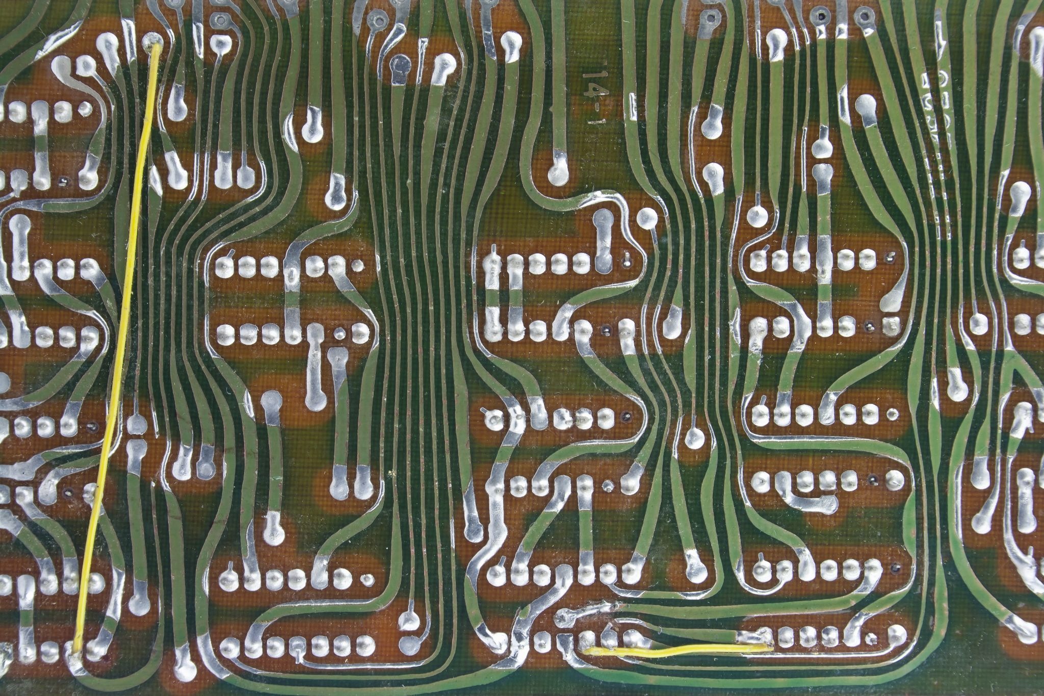 Backside of an old hand-taped printed circuit board, with copper traces curving at freeform, non-45-degree angles between rows of silver solder pads.
