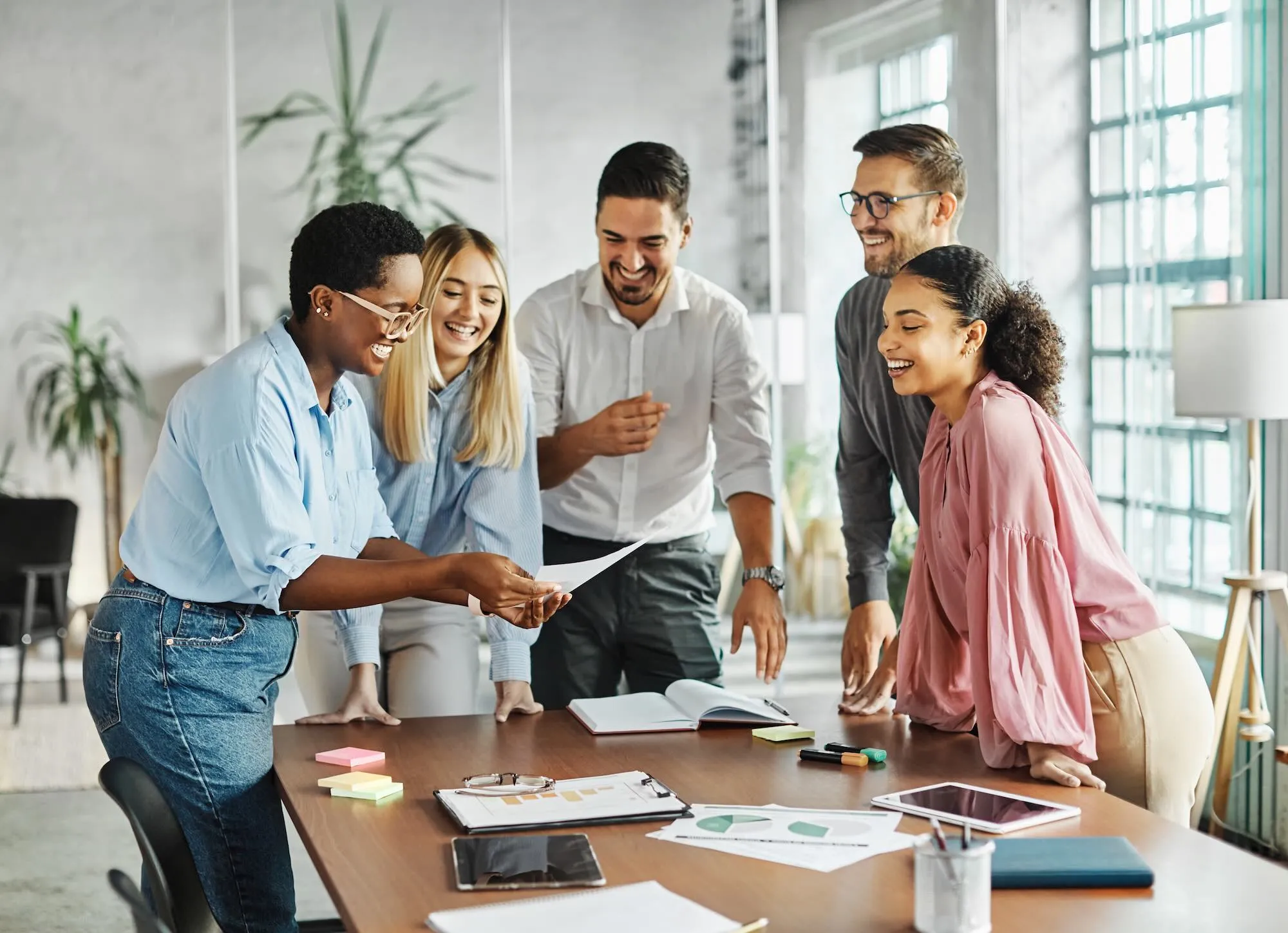 Diverse group of professionals smiling and collaborating around a table in a modern office.