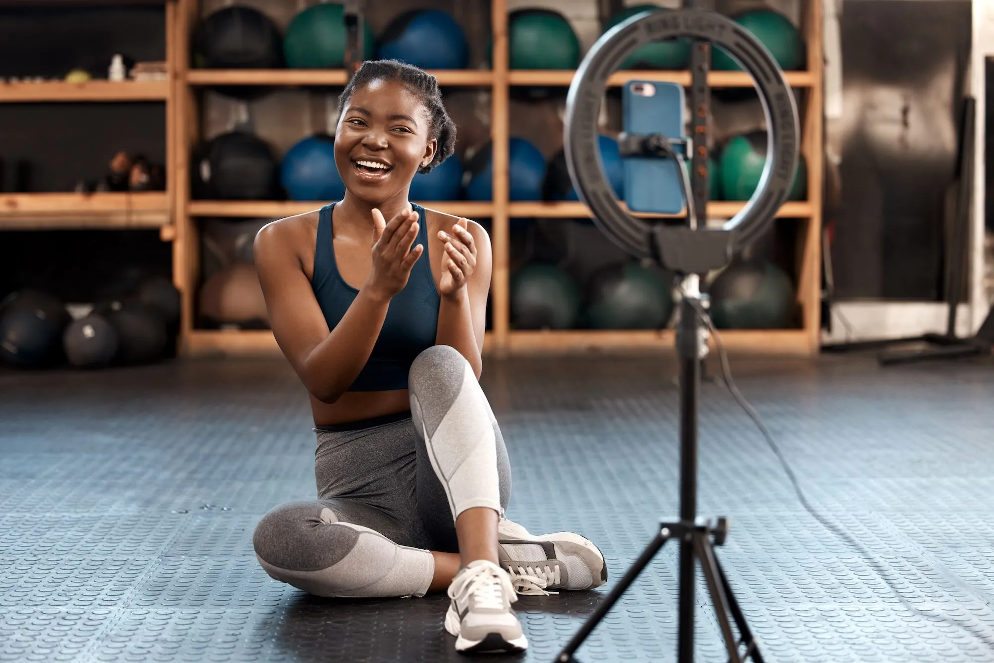 Fitness influencer filming workout content with smartphone and ring light in a gym.