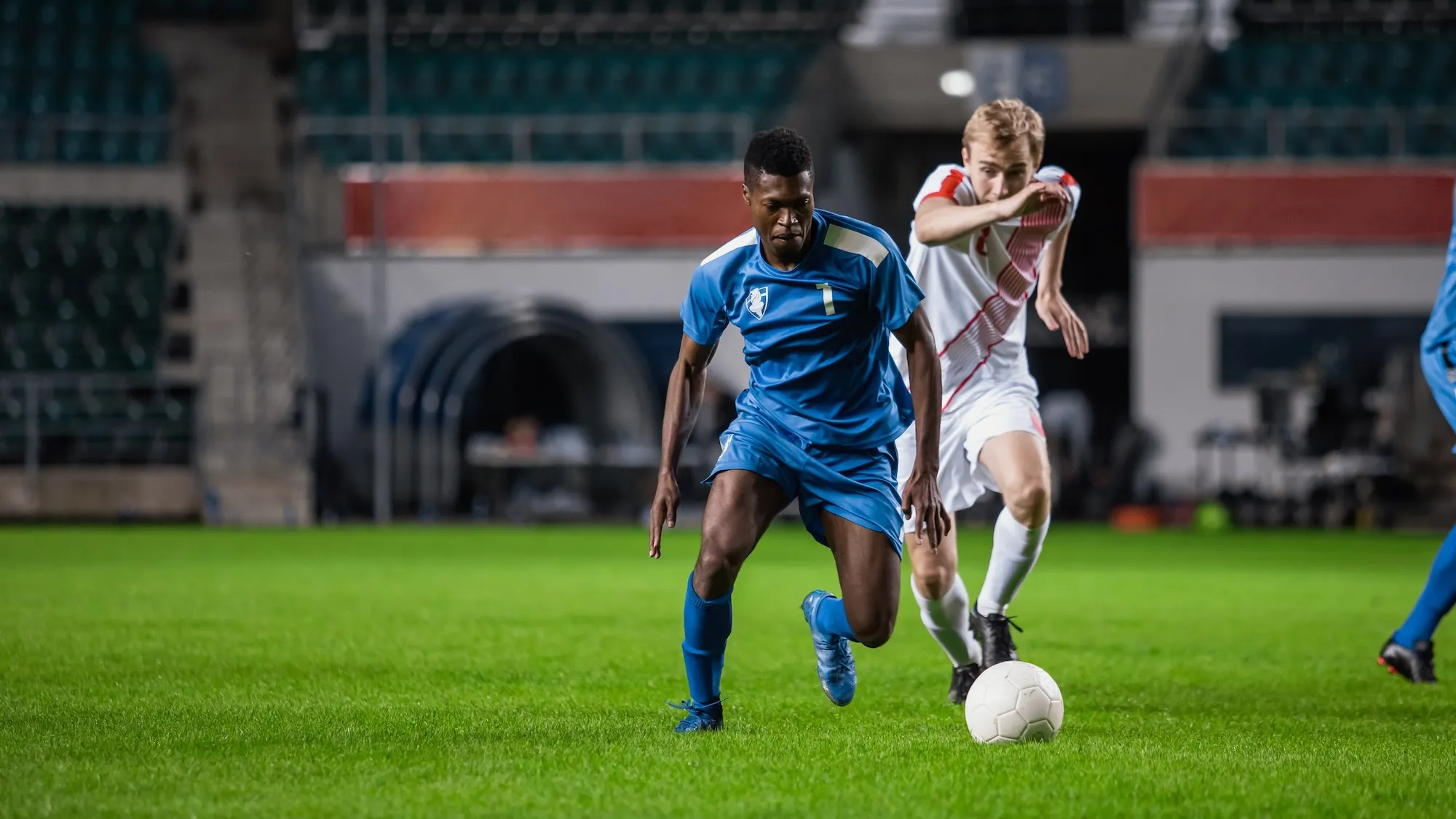 Soccer player in blue uniform dribbling the ball past an opponent during a night game.