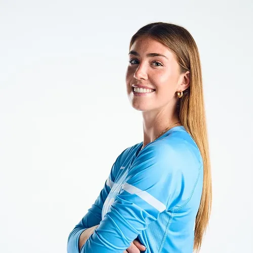 Young woman with long blonde hair smiling and wearing a blue sports jersey against a white background.