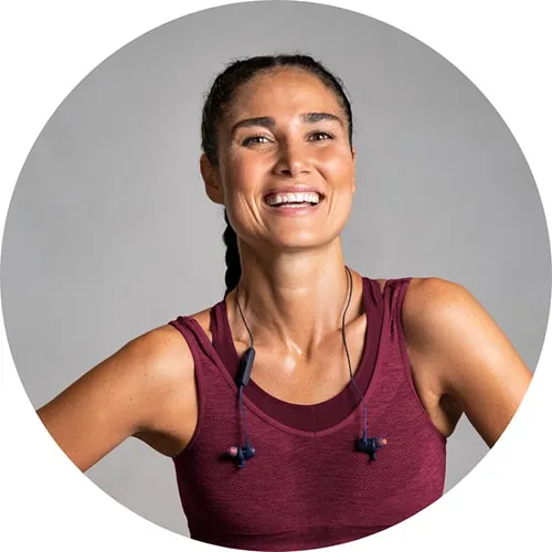 Smiling woman in a maroon athletic top with wireless earphones around her neck.