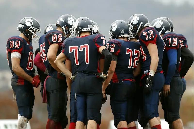 High school football players in navy blue uniforms with white paw prints on helmets huddled together on the field.
