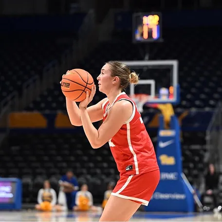 Female basketball player in red uniform preparing to shoot the ball on an indoor court.