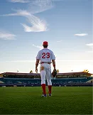 Baseball player wearing number 23 stands on field facing the stadium during sunset.