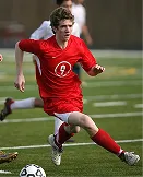 Soccer player in red uniform running to kick the ball on a green field during a match.