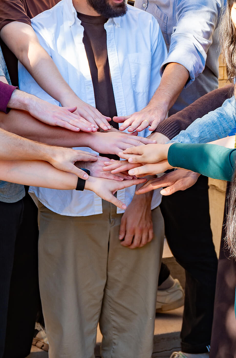 A group of people placing their hands together in a team gesture.